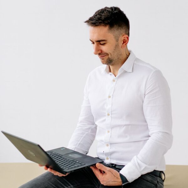 Olaf Nowicki, fizjoterapeuta z Poznania, prowadzi konsultację online z pacjentem, siedząc z laptopem na kolanach.